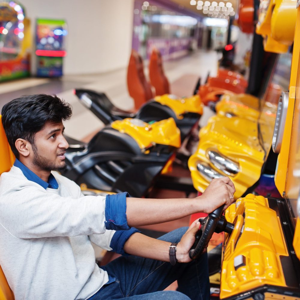 Asian guy compete on speed rider arcade game racing simulator machine.